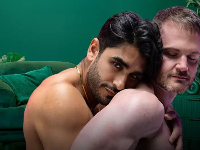 Two shirtless men embracing closely, one resting his head against the other's shoulder